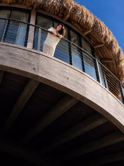 Terraza circular de madera de un bungalow, vista desde abajo, con una persona apoyada en la baranda.