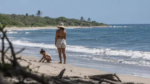 Una mujer y un niño en la orilla, frente a una playa bordeada de vegetación.