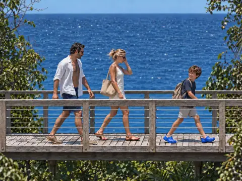 Una familia camina por un puente de madera frente al mar.