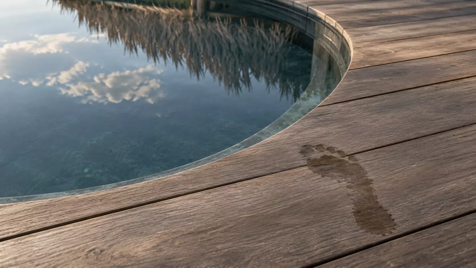 Huella mojada sobre la madera junto al borde curvo de un jacuzzi.
