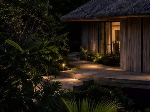 Entrada de un bungalow de madera de noche, con un camino iluminado entre la vegetación.