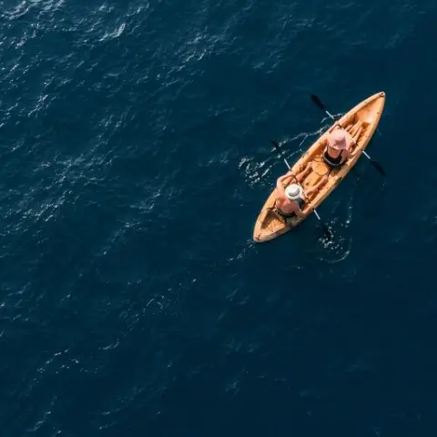Vista cenital de un kayak con dos personas remando sobre el mar azul profundo.