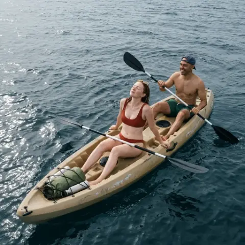 Una pareja en un kayak doble sobre el mar; ella descansa con los ojos cerrados y él rema sonriendo.
