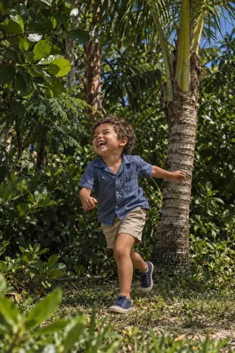 Un niño corre riendo entre palmeras y vegetación.