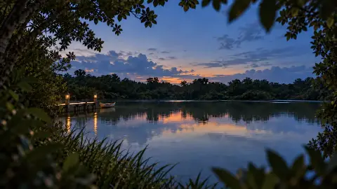 La laguna al anochecer, con un muelle iluminado y la vegetación enmarcando la vista.