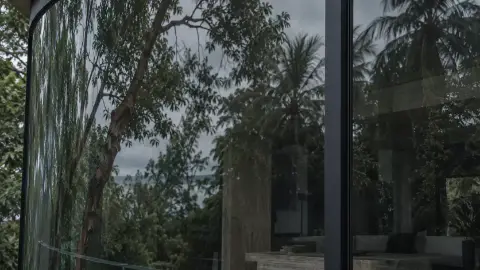 Un ventanal de vidrio refleja los árboles y las palmas que rodean el bungalow.