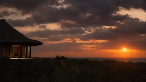 Silueta de un bungalow de techo de palma frente al sol del atardecer sobre el mar.