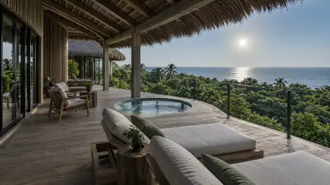 Terraza de madera bajo techo de palma, con tumbonas, un jacuzzi y el mar al fondo.